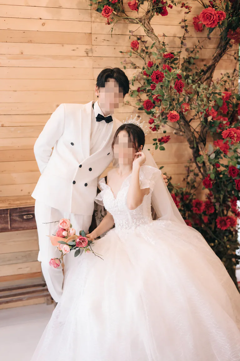 흰 예복을 입은 두 사람이 장미 장식 앞에 있는 모습